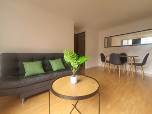 A modern living room with a dark grey sofa, green cushions, a round wooden coffee table, and a potted plant. - Charming 2-bedroom Apartment in Medellín's Golden Mile (Medellín)