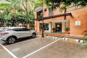 A parking area with a white car, a building with a brick facade, and a sign that reads 'DASING'. - Charming 2-bedroom Apartment in Medellín's Golden Mile (Medellín)