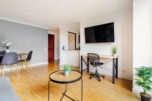 Ein modernes Wohnzimmer mit Essbereich, einem an der Wand montierten Fernseher und einem kleinen runden Tisch mit einer Pflanze.
