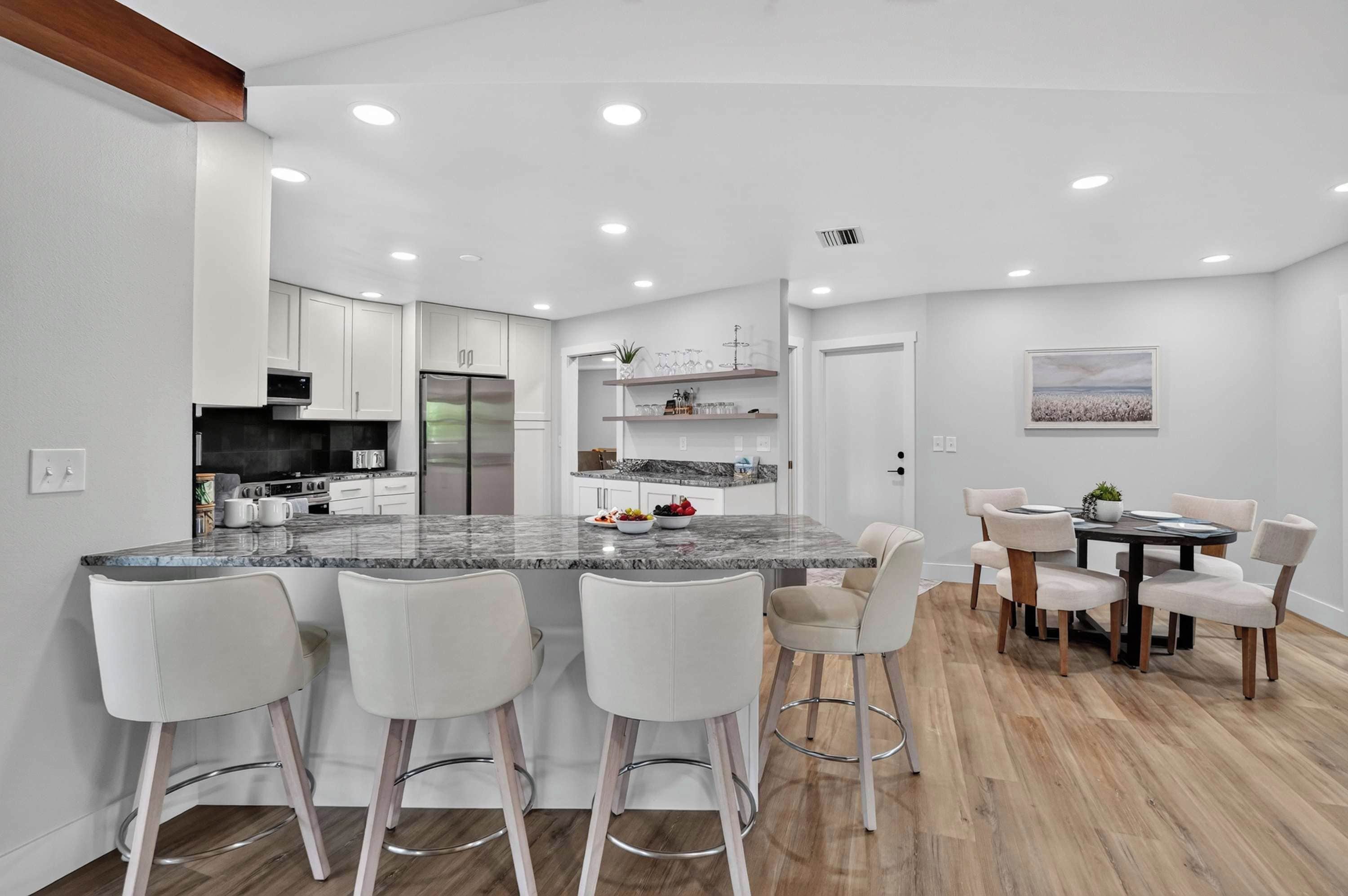 A modern kitchen with a marble island, bar stools, and a dining area with a wooden table and chairs.