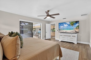 A bedroom with a bed, a ceiling fan, a television on a dresser, and a sliding glass door leading to an outdoor area. - The Pool. The Views. The House. (Sarasota)