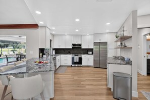 A modern kitchen with white cabinets, stainless steel appliances, and a marble countertop. - The Pool. The Views. The House. (Sarasota)