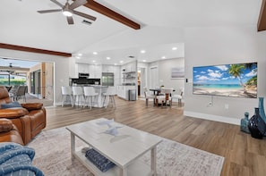 A spacious living area with a dining table, a kitchen in the background, and a beach-themed painting on the wall. - The Pool. The Views. The House. (Sarasota)