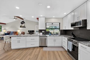 A modern kitchen with white cabinets, a built-in oven, a microwave, and a large island with a sink. - The Pool. The Views. The House. (Sarasota)