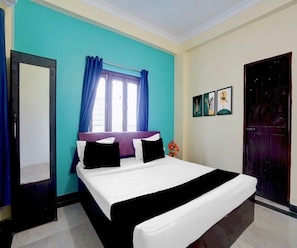 A hotel room with a bed, a window with curtains, a door, and wall art. - Classic Hotel Royal Brothers Stay (Danapur)