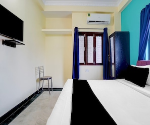 A hotel room with a bed, a chair, an air conditioner, and a window with curtains. - Classic Hotel Royal Brothers Stay (Danapur)