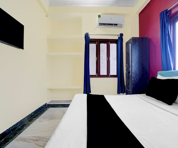 A hotel room with a bed, a wardrobe, a window with curtains, and an air conditioning unit.