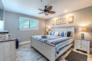A bedroom with a bed, a nightstand, a desk, a ceiling fan, and a window with blinds. - 2BR Resort Escape - Pools and Bars (Hilton Head Island)