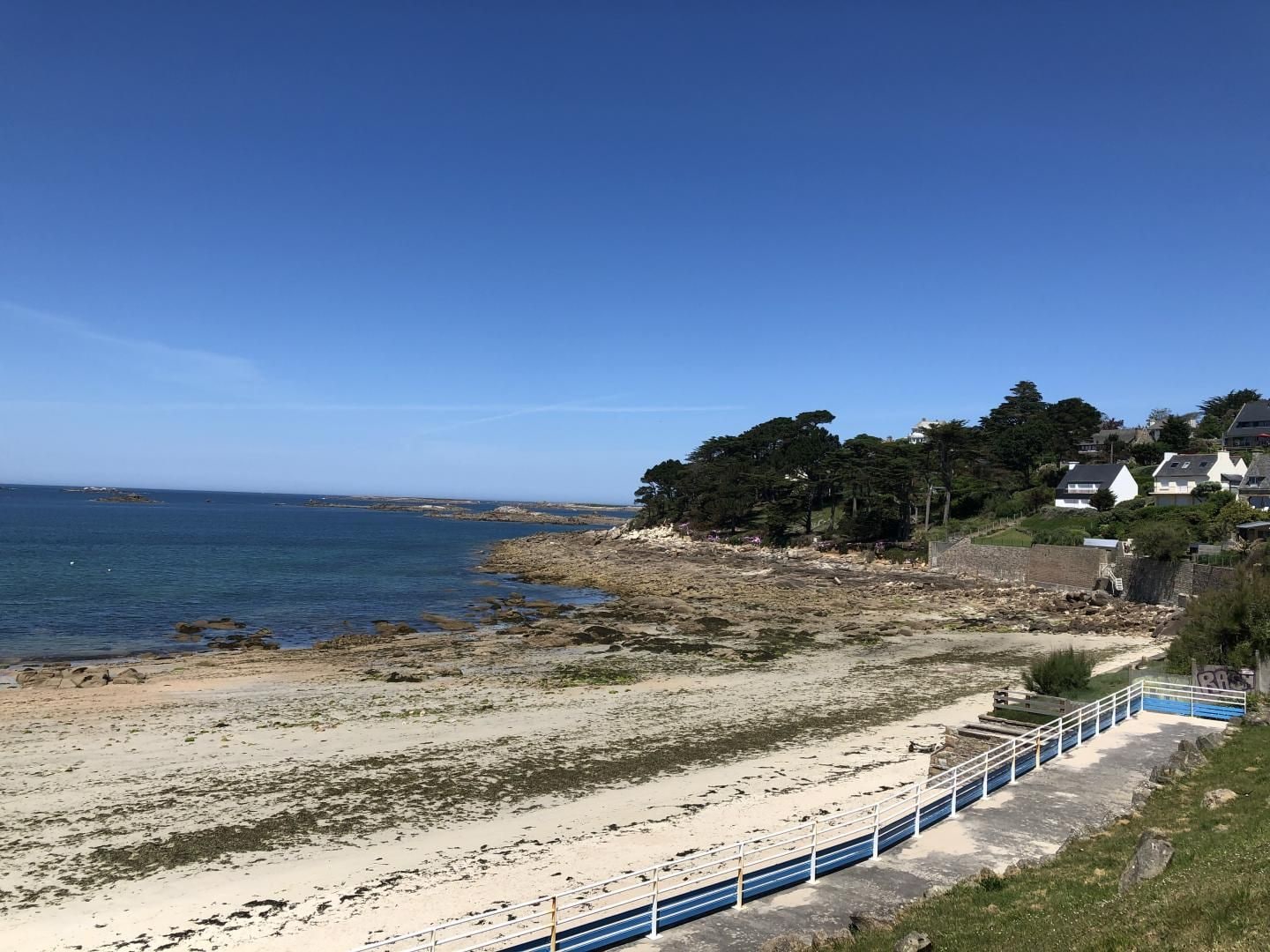 Une vue sur la côte, avec une plage de sable, un ciel bleu dégagé et une rangée de maisons le long du rivage.
