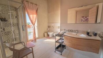 A bathroom with a large sink, a toilet, a shower with a glass door, and a chair.