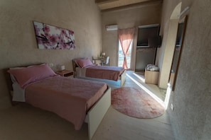 A bedroom with two beds, a TV, and a window with curtains.
