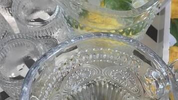 Une carafe en verre transparent contenant des tranches de citron et des feuilles de menthe, posée sur une table à motifs floraux.