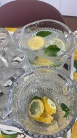 Un jarro de vidrio transparente con rodajas de limón y hojas de menta, sobre una mesa con estampado floral.