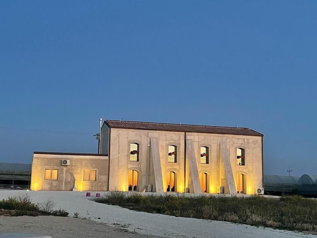 A building with multiple arched openings and a flat roof, situated in a desert-like environment with sparse vegetation.