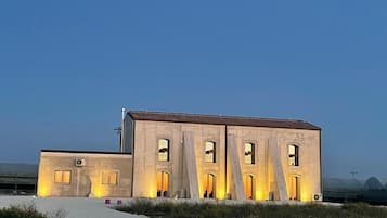A building with multiple arched openings and a flat roof, situated in a desert-like environment with sparse vegetation.