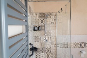 A shower area with patterned tiles, a glass door, and a towel rack. - B&B U'Minnulitu SALPIETRO (Caltagirone)