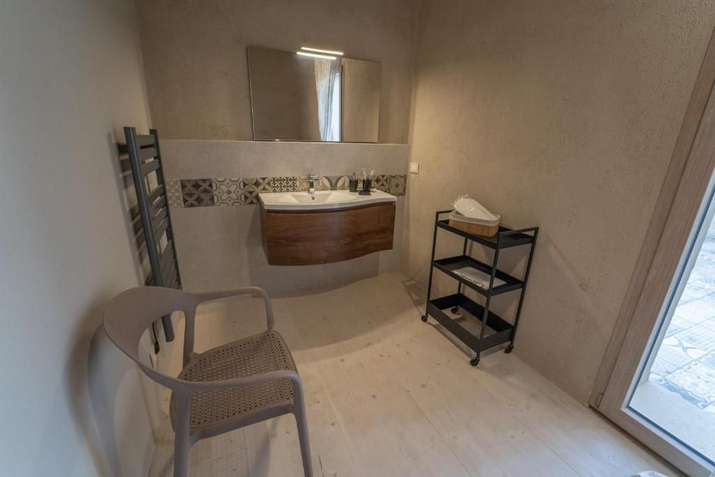 Un bagno con lavandino, specchio, portasci, sedia e scaffale.