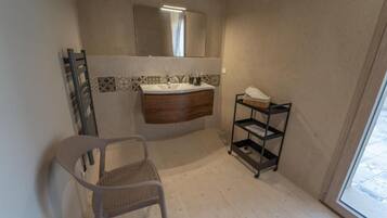 Un bagno con lavandino, specchio, portasci, sedia e scaffale.