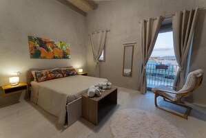 A bedroom with a bed, bedside tables, a chair, a window with curtains, and a painting on the wall.