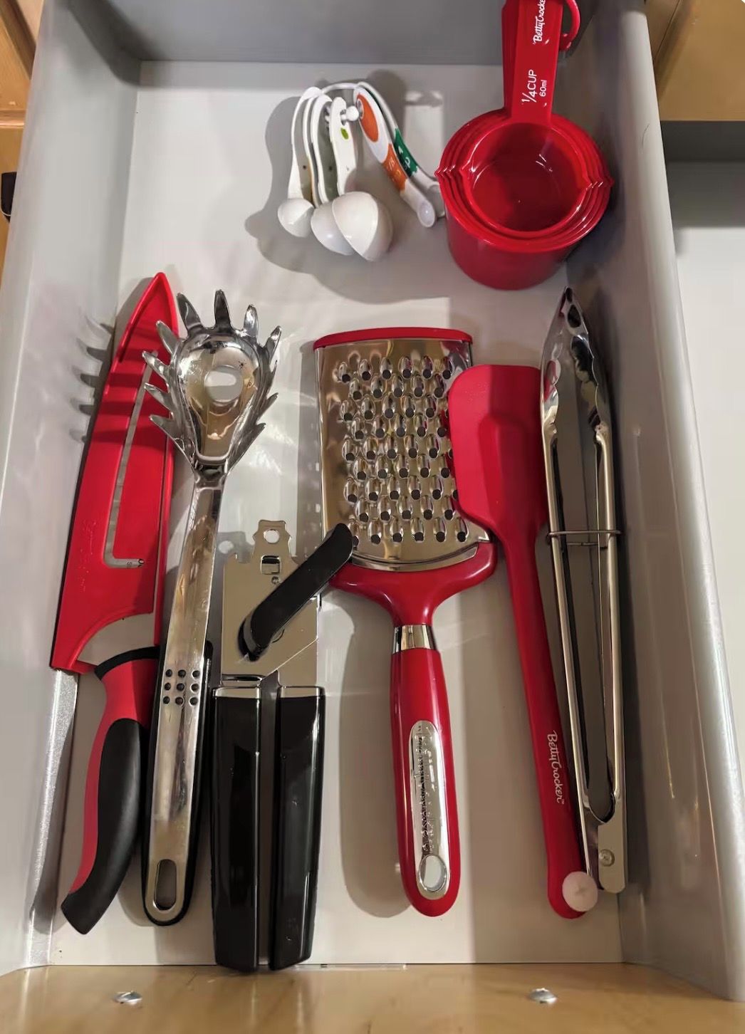 A drawer containing various kitchen utensils including a grater, a grater with holes, a grater with a red handle, a grater with a black handle, a grater with a red handle, a grater with a black handle, a grater with a red handle, a grater with a black handle, a grater with a red handle, a grater with a black handle, a grater with a red handle, a grater with a black handle, a grater with a red handle, a grater with a black handle, a grater with a red handle, a grater with a black handle, a grater with a red handle, a grater with a black handle, a grater with a red handle, a grater with a black handle, a grater with a red handle, a grater with a black handle, a grater with a red handle, a grater with a black handle, a grater with