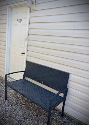 A metal bench outside a building with a door labeled 'Basement Suite.'