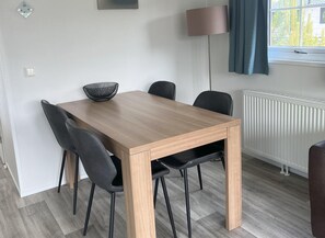 A dining area with a wooden table, four chairs, a black woven bowl, a lamp, and a window with curtains.
