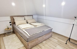 Una camera da letto ordinata con un letto, cuscini, un comodino e una lampada da terra.