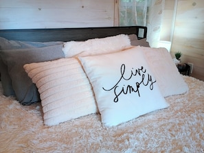 Una cama con ropa de cama y almohadas mullidas, una de ellas con el texto 'live simply'.