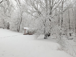 A snow-covered forest with a wooden structure and a bench.