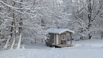 En hyggelig hytte med veranda, omgivet af sneklædte træer.