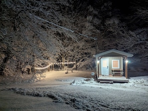 A small cabin with a porch, surrounded by snow-covered trees and a string of lights.