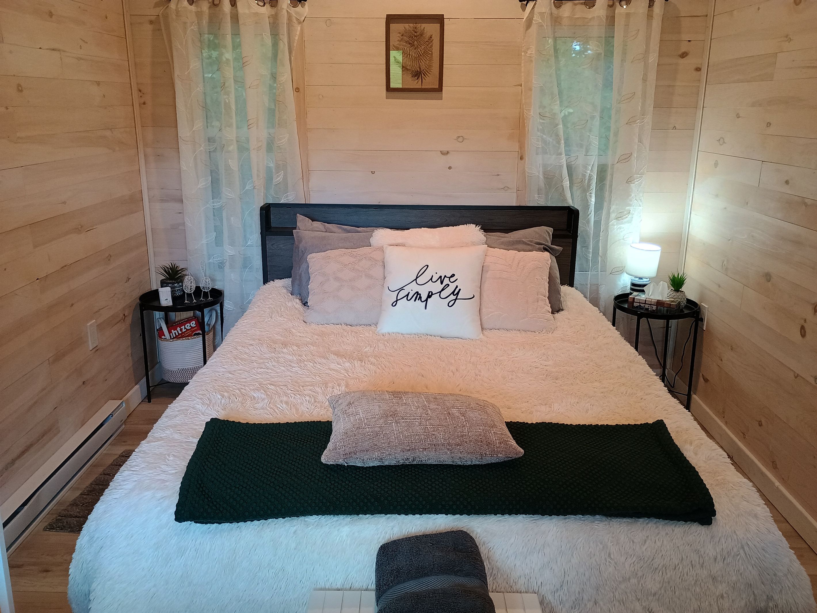 Une chambre à coucher avec un lit, des oreillers, une table de chevet, une lampe et un tableau encadré au mur.