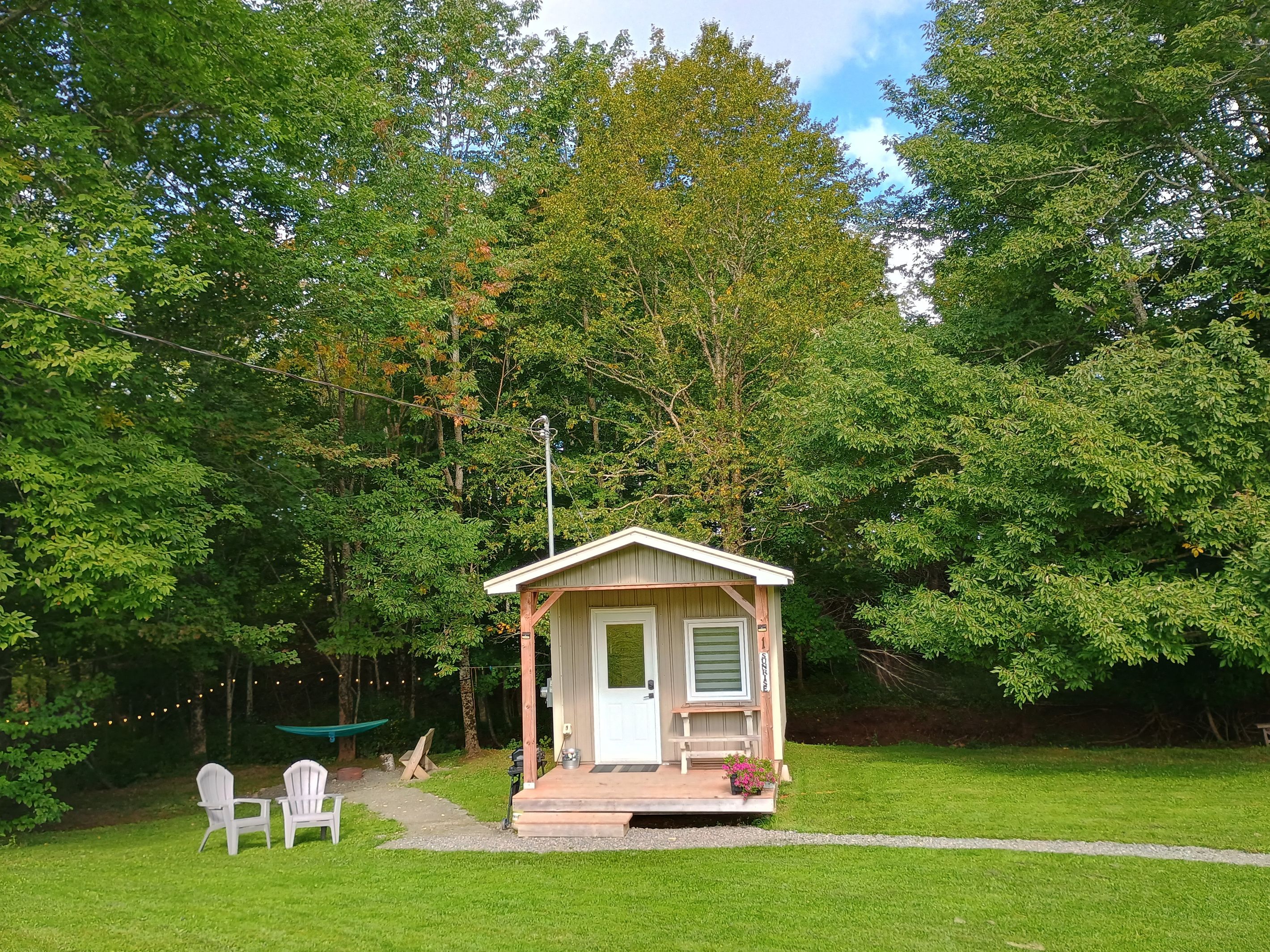 A small wooden cabin with a porch, surrounded by a well-maintained lawn and dense trees.