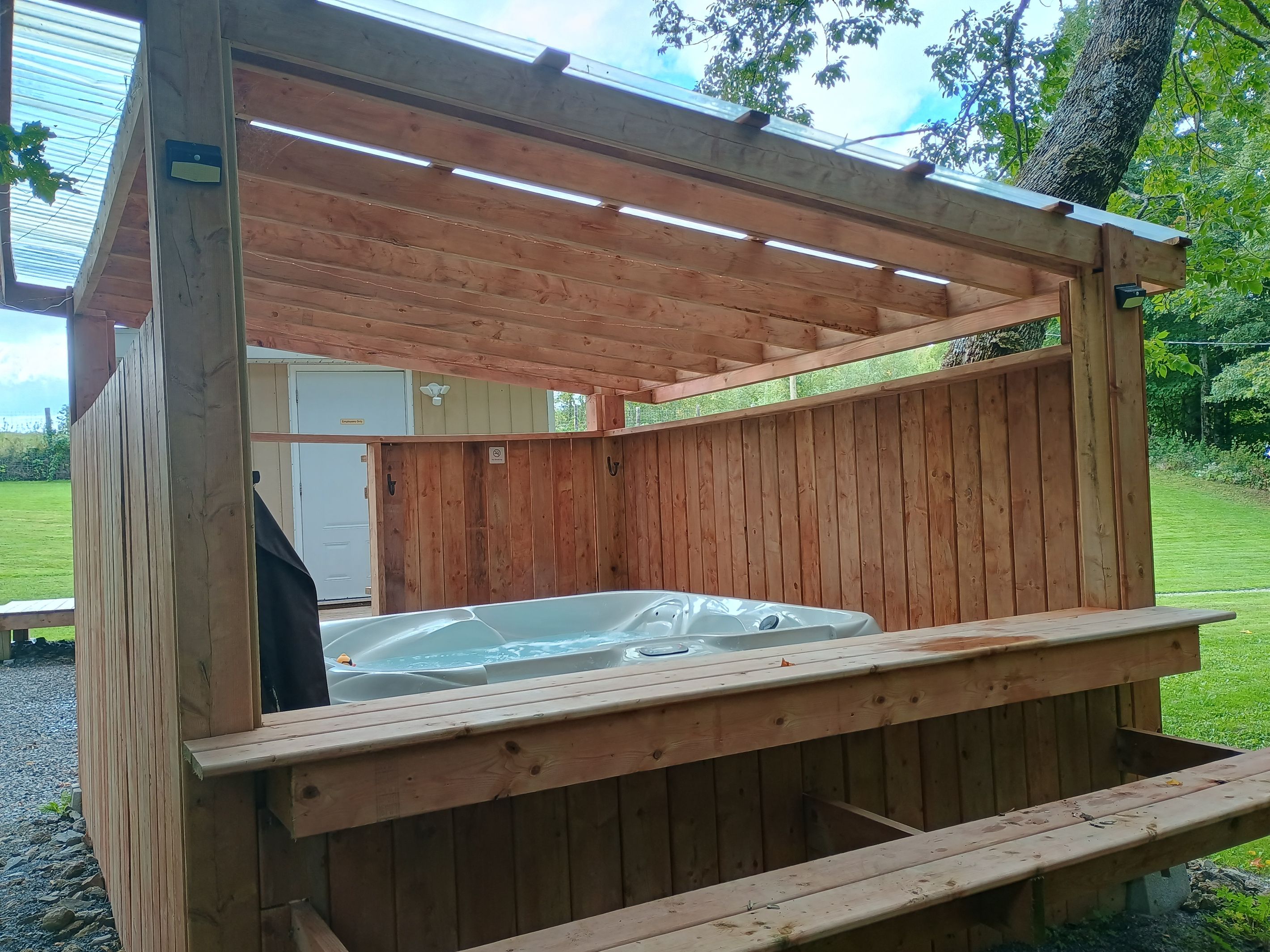 A wooden hot tub enclosure with a bench, surrounded by a wooden deck.