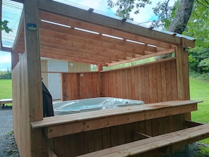 Estructura de madera para bañera de hidromasaje con un banco, rodeada por una terraza de madera.