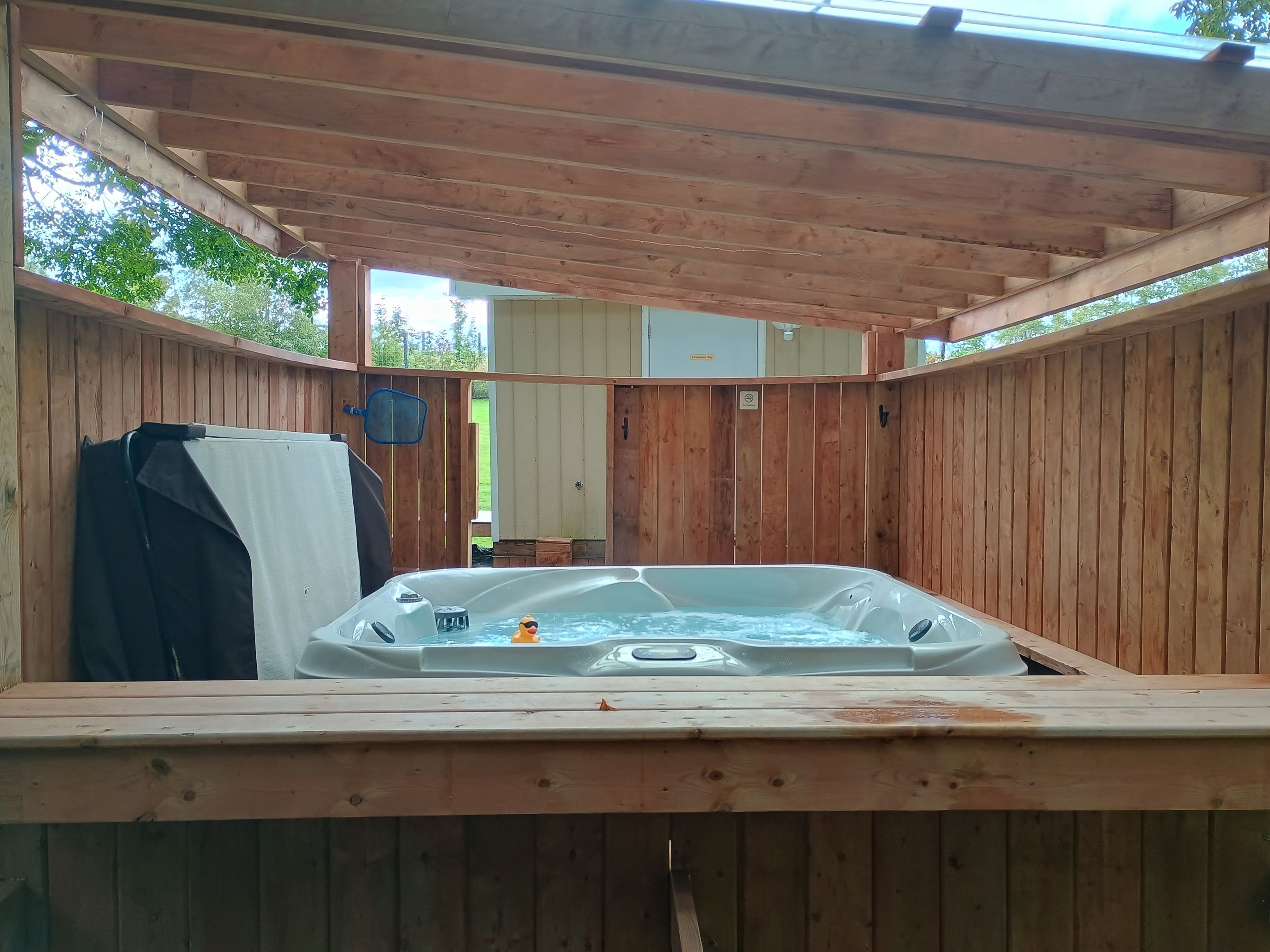 Un bain à remous en bois, doté d’un couvercle, entouré de murs en bois et surmonté d’un plafond en bois.