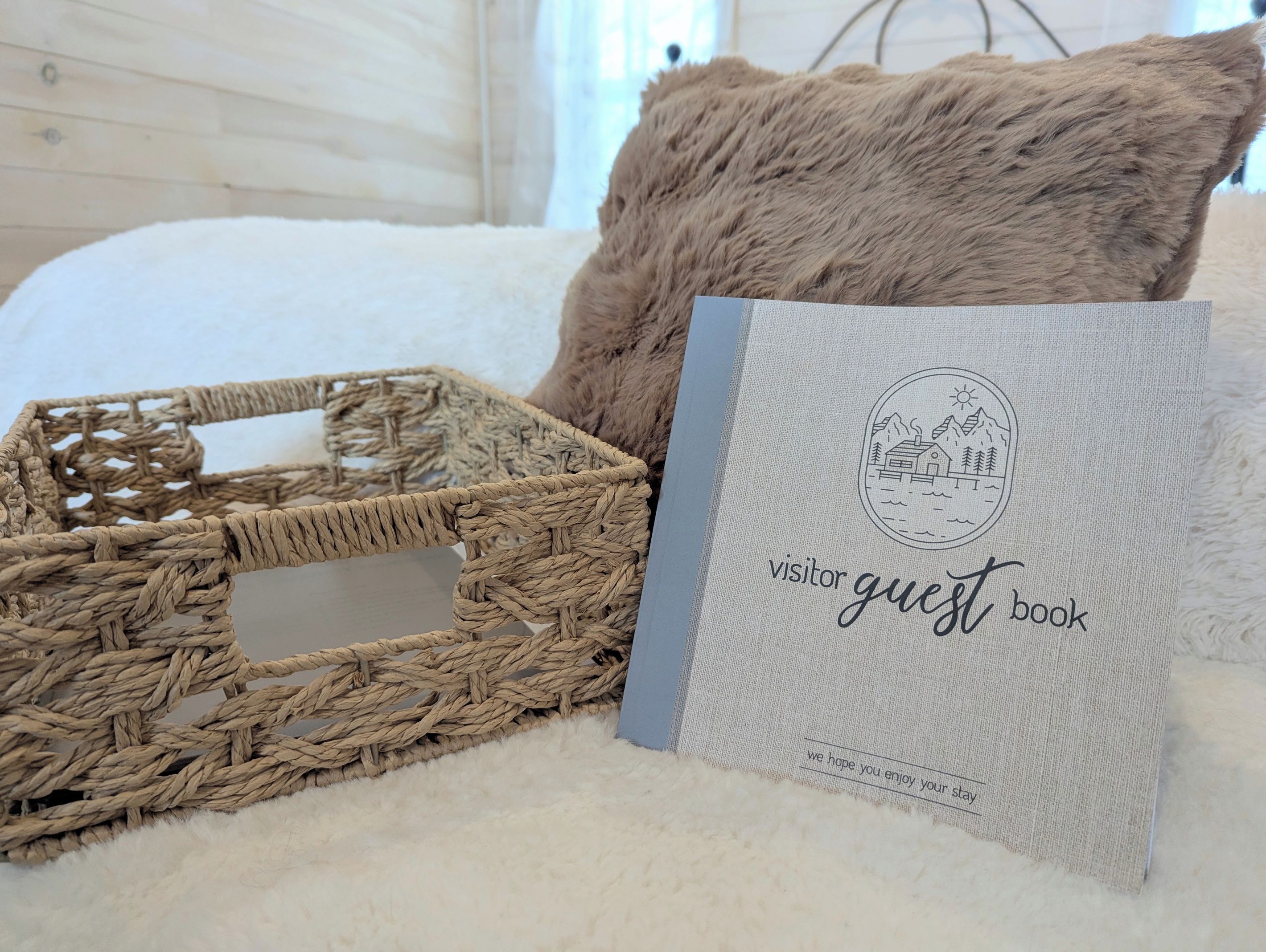 Un panier en osier, un coussin moelleux et un livre d’or posés sur une surface blanche à texture.