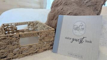 Un panier en osier, un coussin moelleux et un livre d’or posés sur une surface blanche à texture.