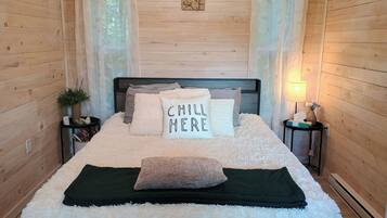 A cozy bedroom with a wooden headboard, a fluffy white bedspread, and a pillow with 'CHILL HERE' text.