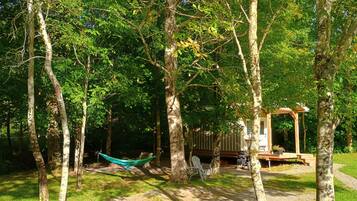 A hammock between trees, a wooden deck, and a picnic table in a wooded area.
