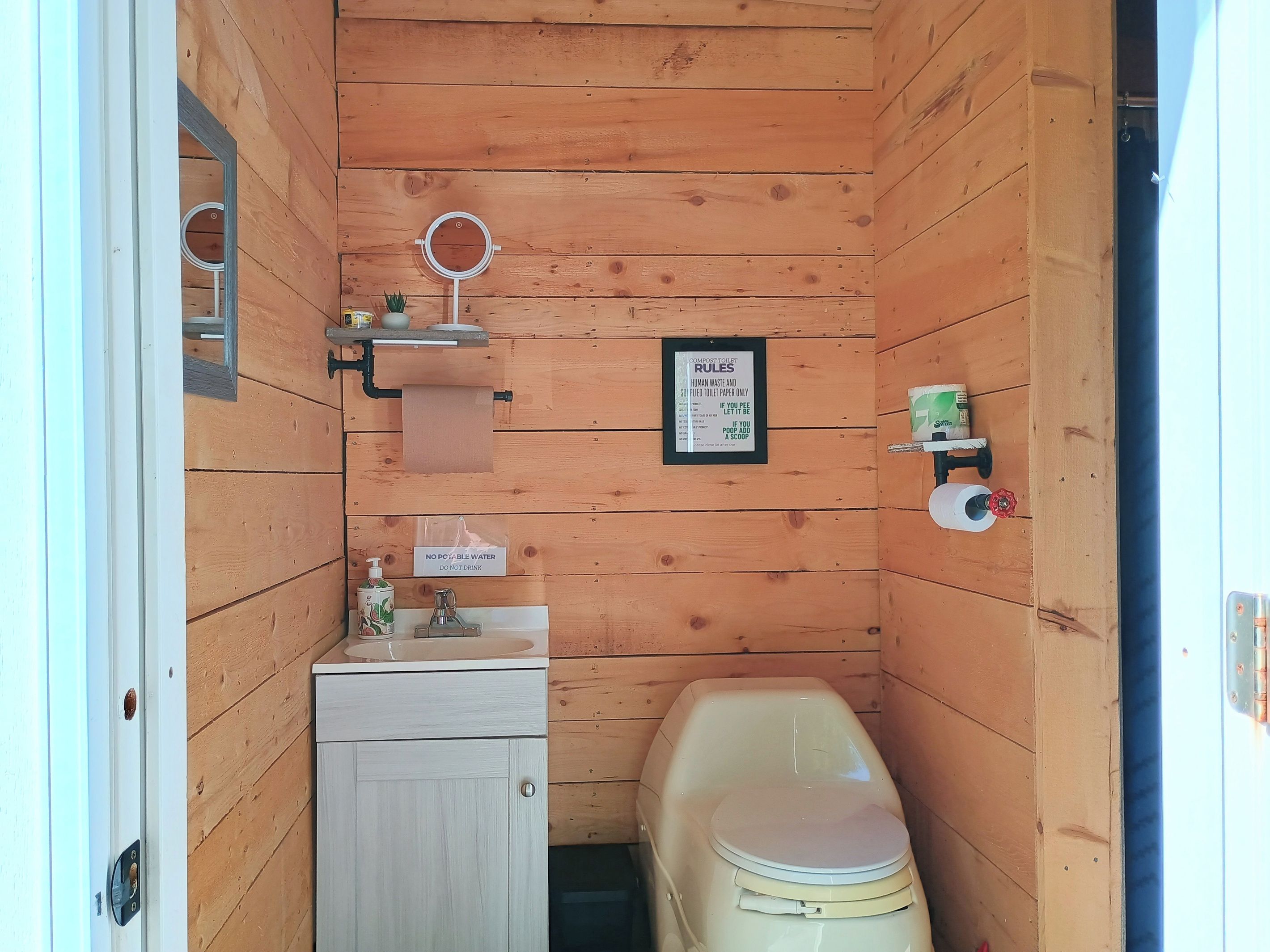 Une petite salle de bain en bois comprenant des toilettes, un lavabo et un miroir.