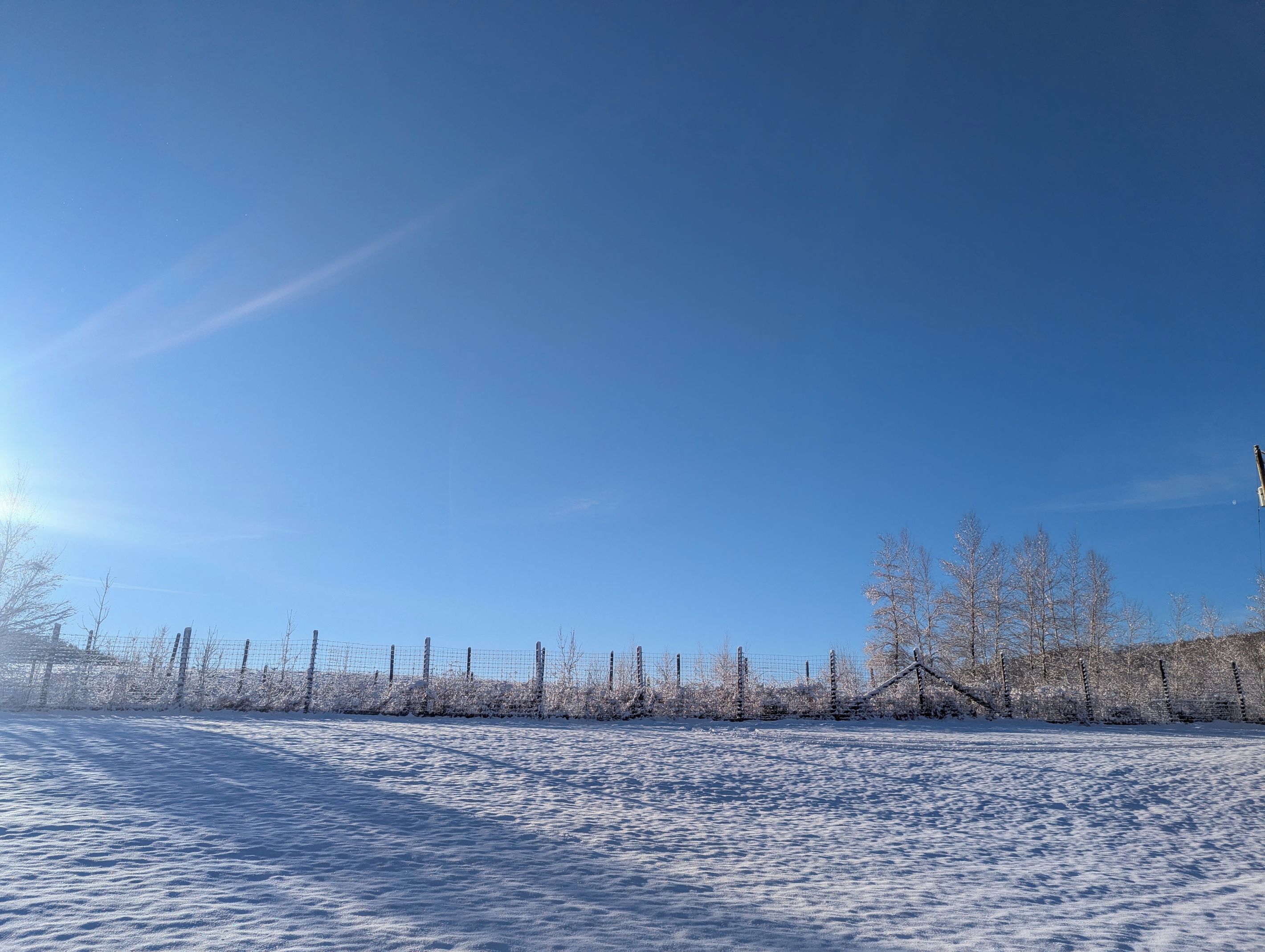 Ett snötäckt landskap med en klar himmel och ett staket i förgrunden.