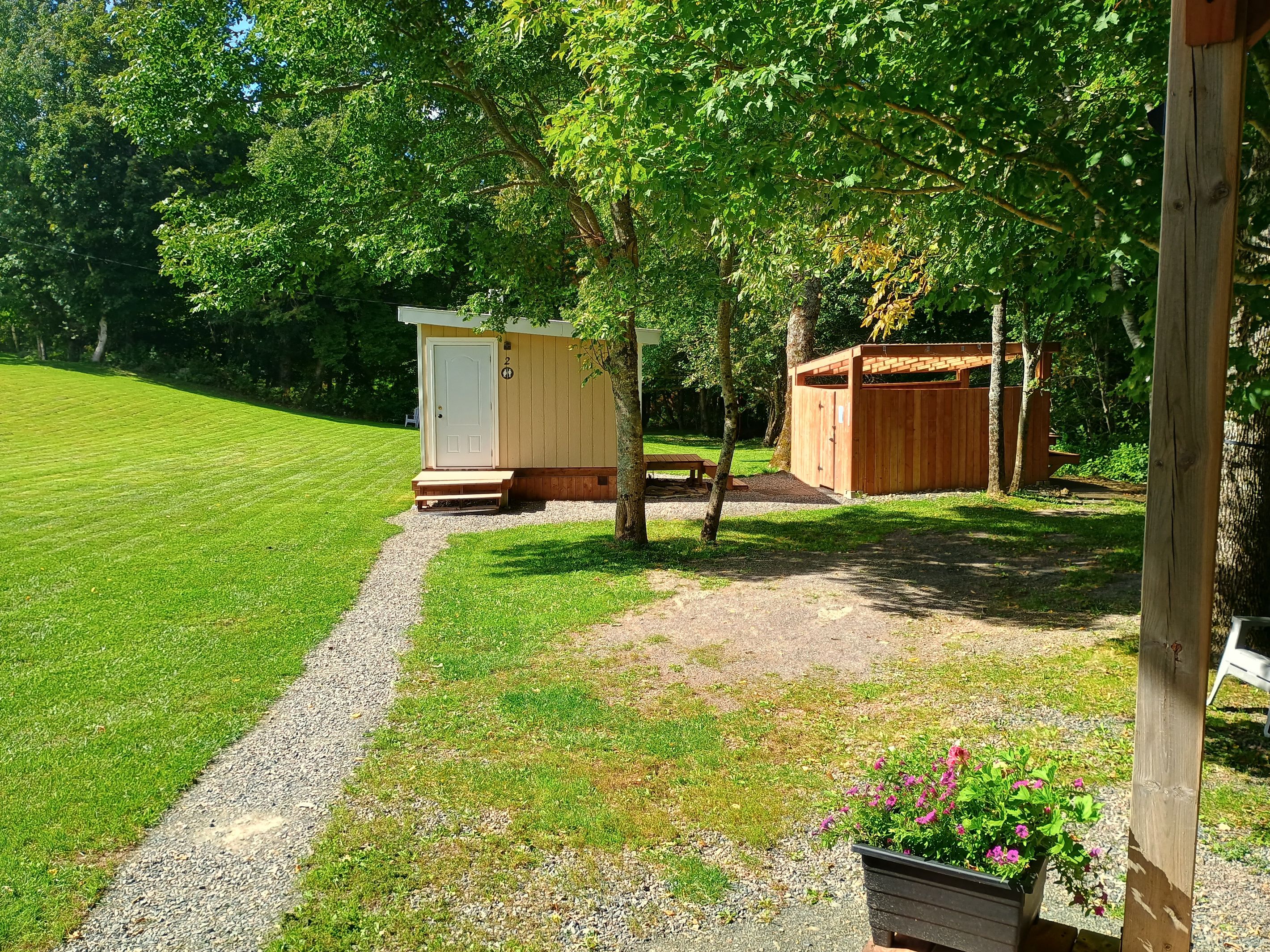A well-maintained grassy area with a gravel path leading to a small wooden structure, possibly a shed or storage, and a larger wooden building with a door and number '2' on the wall.