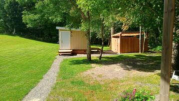 A well-maintained grassy area with a gravel path leading to a small wooden structure, possibly a shed or storage, and a larger wooden building with a door and number '2' on the wall.