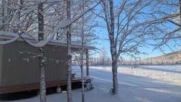 A snow-covered outdoor area with a wooden structure, possibly a shed or a small cabin, and a metal fence in the background.