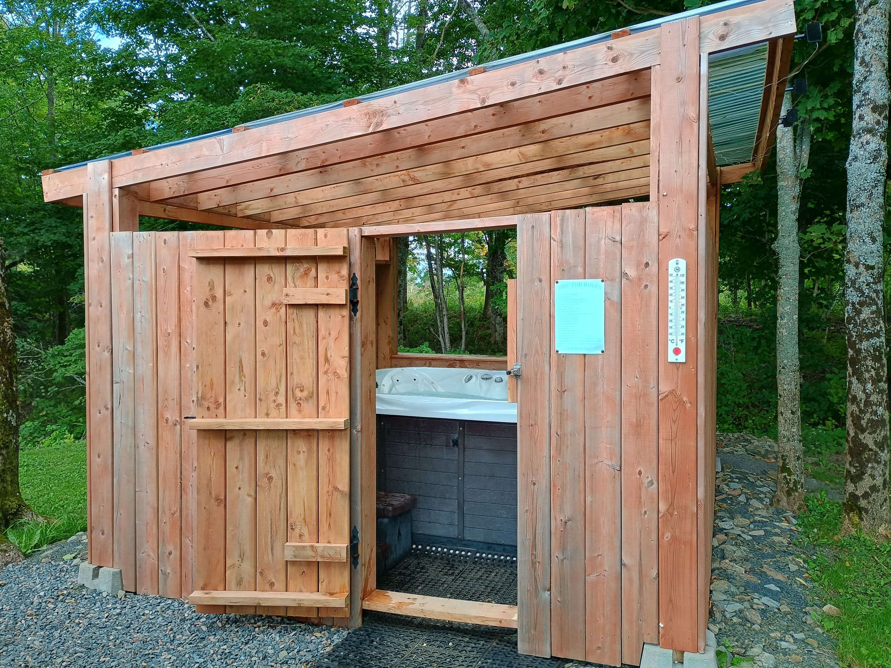 A wooden cabin with a door open, revealing a hot tub inside.