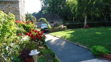 Un sentier de jardin mène à un bâtiment en pierre, avec une voiture garée à proximité.