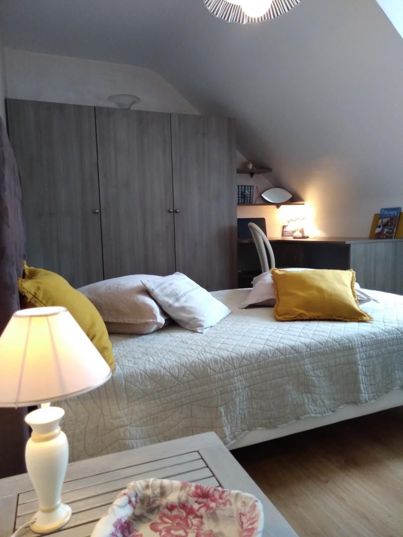 Ein Schlafzimmer mit einem Bett, Kissen, einem Nachttisch, einer Lampe und einem Schreibtisch mit Stuhl.