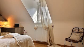 Une chambre avec un plafond en pente, un lit avec une literie blanche, une chaise avec un coussin et un rideau.