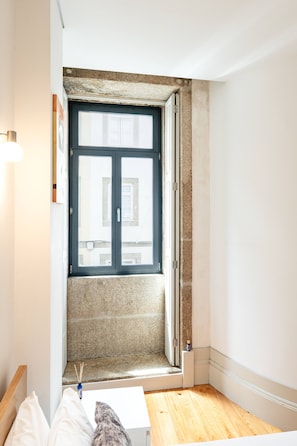 Une pièce avec une grande fenêtre, un plancher en bois et un mur blanc.